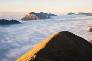 mehr Motivation & Durchhaltevermögen für große Ziele symbolisiert durch einen Mann auf einem Berggipfel über den Wolken